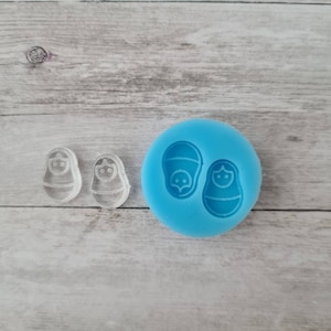 Pode incluir: Um molde transparente para bonecas Matrioska e duas figuras de bonecas. O molde de silicone azul tem duas impressões de bonecas. As bonecas têm uma forma arredondada com cabeça e corpo. As figuras são transparentes.