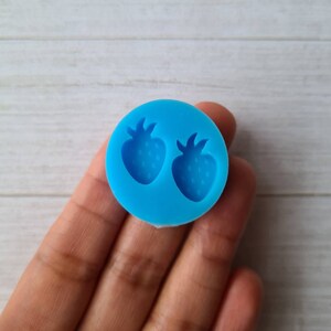 May include: A vibrant blue silicone mould with two strawberry designs. The circular mould has a smooth surface with detailed strawberry impressions. The strawberries have textured surfaces and green stems. Suitable for crafts or baking.