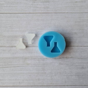 May include: A light blue silicone mould with two funnel shapes and two white, plastic funnel shapes. The items are on a light wood grain surface. The mould is round and the funnels are in different sizes.