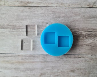 May include: A clear, square-shaped resin mold with two square cavities, next to two clear, square resin pieces. The mold is a bright blue color and sits on a light wood-grain surface. The resin pieces are transparent.