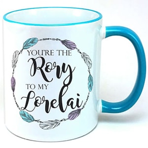 May include: White ceramic mug with a turquoise rim and handle. The mug features a black and white graphic of a feather wreath with the text "You're the Rory to my Lorelai".