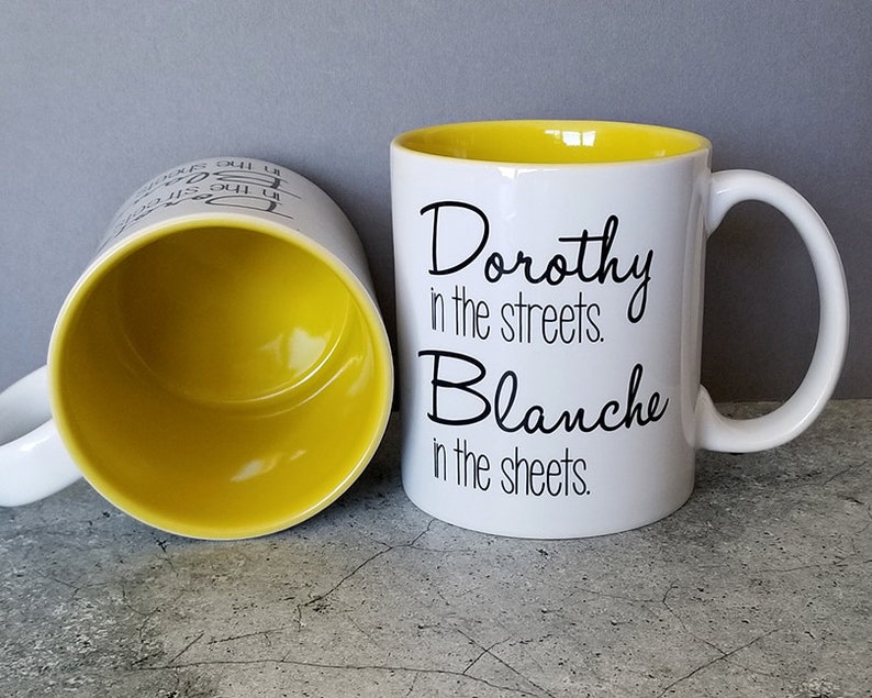 May include: White ceramic mug with a yellow interior and black text that reads "Dorothy in the streets. Blanche in the sheets."