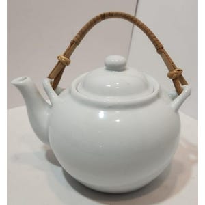 Puede incluir: Tetera de cerámica blanca con asa y tapa de bambú trenzado.