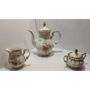May include: A white porcelain tea set with gold trim and floral designs. The set includes a teapot, creamer, and sugar bowl.