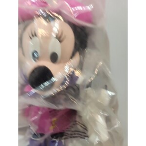 May include: A pink and white Minnie Mouse plush toy in a clear plastic bag. The toy has a pink bow and black eyes.