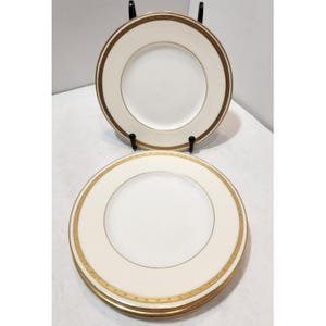 Puede incluir: Un juego de platos de porcelana blanca con un borde dorado y marrón. Los platos tienen un diseño simple y elegante, con una banda dorada ancha y una banda marrón más delgada alrededor del borde. Los platos están apilados.