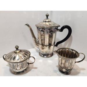 May include: A silver tea set with a coffee pot, sugar bowl, and creamer. The coffee pot has a black handle and a lid with a finial. The sugar bowl has a lid and two handles. The creamer has a handle.