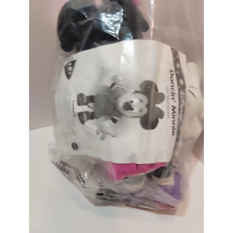May include: A black and white plush toy of Minnie Mouse in a cheerleader outfit. The toy is packaged in a clear plastic bag with a white label that says "Disney's Dancin' Minnie" and "Soft Touch Plush".
