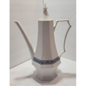 Può includere: Teiera in ceramica bianca con un motivo a foglie blu e bianco intorno al centro. La teiera ha un beccuccio alto e sottile e un coperchio con una punta appuntita.