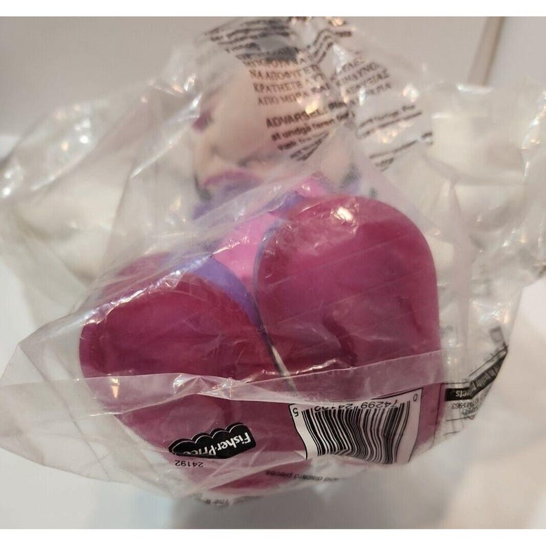 May include: A pair of purple and pink children's shoes in a plastic bag with a Fisher-Price label. The shoes are packaged for sale.