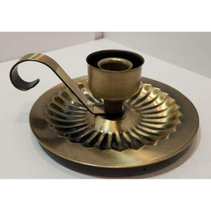 May include: A gold metal candle holder with a fluted base and a curved arm. The holder has a simple design and is perfect for adding a touch of elegance to any home.