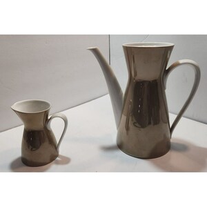 May include: A white and brown ceramic teapot and creamer set. The teapot has a tall, slender body and a curved spout. The creamer is a smaller, rounder pitcher with a handle.