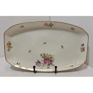 May include: An off-white, rectangular serving platter with a gold trim and floral designs. The platter features clusters of pink, purple, and yellow flowers. The flowers are scattered across the surface.