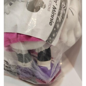 May include: A plush Minnie Mouse toy wearing a pink dress and black shoes. The toy is packaged in a clear plastic bag with a Disney label that says "Disney's Minnie".