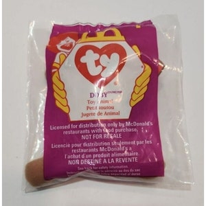May include: A brown plush toy dog named "Dosy" in a clear plastic bag with a pink and yellow Ty Beanie Baby tag. The tag reads "Toy Animal! Petit toutou Jugete de Animal". The bag also has text that reads "Licensed for distribution only by McDonald's restaurants with food purchase. NOT FOR RESALE. Licencié pour distribution seulement par les restaurants McDonald's à l'achat d'un produit alimentaire. NON DESTINE A LA REVENTE."