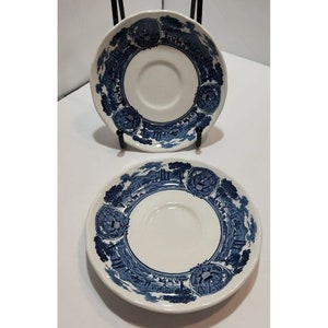 Puede incluir: Dos platillos de cerámica azul y blanco con un patrón decorativo de una escena de paisaje. Los platillos son perfectos para el té o el café.