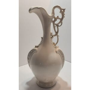 May include: White ceramic jug with an ornate, scrolled handle. The jug has a round body and a delicate, floral design.