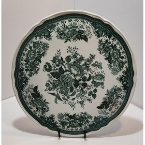 Puede incluir: Un plato grande de cerámica blanca con un patrón floral verde. El plato tiene un borde festoneado y un centro elevado.