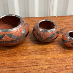 May include: Three terracotta pottery bowls with black geometric designs. The bowls are nested, with the largest bowl at the front and the smallest bowl at the back.