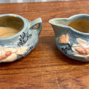 May include: A blue and white ceramic creamer and sugar bowl set with floral designs. The creamer has a handle and a spout. The sugar bowl has two handles.