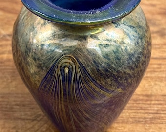 May include: A small blue glass vase with gold and green swirling patterns. The vase has a wide mouth and a rounded body.