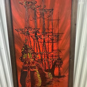 May include: A framed painting featuring three sailing ships with detailed rigging, set against a vivid red backdrop. The ships are rendered in dark hues, creating a strong contrast. The artwork is enclosed within a dark brown wooden frame.