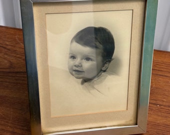 May include: A black and white photograph of a baby in a silver frame. The baby is looking to the right and smiling.