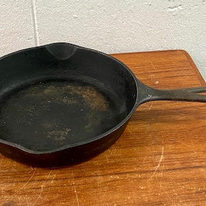 May include: A black cast iron skillet with a long handle. The skillet is on a wooden surface.