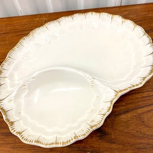 以下が含まれることがあります： 波打つ縁取りと金色の縁取りが付いた白いセラミック製のサービングディッシュ。ディッシュは2つのセクションに分かれており、片方がもう片方よりも大きい。