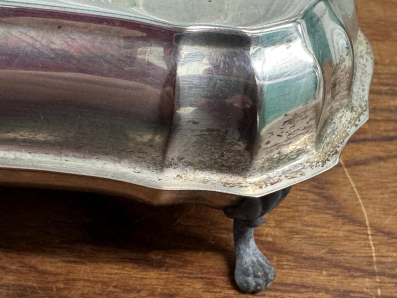 Puede incluir: Bandeja de servir de plata con borde festoneado y tres patas. La bandeja tiene un aspecto desgastado y envejecido.