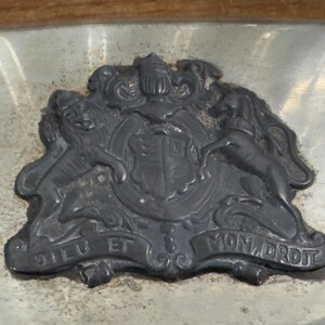 Puede incluir: Una bandeja de plata con un dise&ntilde;o en relieve detallado de un escudo de armas. El escudo de armas presenta dos leones, un unicornio y un escudo con una corona. El texto "Dieu et Mon Droit" est&aacute; inscrito en la parte inferior del dise&ntilde;o.