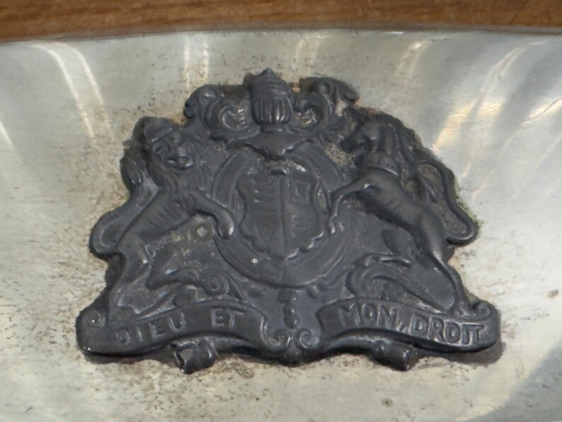 Puede incluir: Una bandeja de plata con un dise&ntilde;o en relieve detallado de un escudo de armas. El escudo de armas presenta dos leones, un unicornio y un escudo con una corona. El texto "Dieu et Mon Droit" est&aacute; inscrito en la parte inferior del dise&ntilde;o.