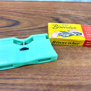 May include: A green plastic pocket binocular with a black focus adjustment knob. The box reads "VP Binocular" and "Vest Pocket or Handbag Binocular".