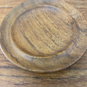 May include: A round wooden coaster with a smooth, dark brown surface and a slightly raised edge.