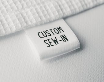 May include: White fabric label with black text that reads "CUSTOM SEW-IN".