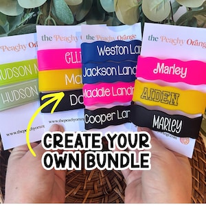 May include: A collection of colourful, wavy silicone wristbands featuring personalised names in white or black text. The bands are displayed on white cards labelled with the Peachy Orange brand name, showcasing various bright colours like neon pink, yellow, and black.