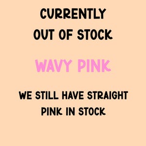 May include: A light peach-coloured sign with black text that reads CURRENTLY OUT OF STOCK, followed by the text WAVY PINK in pink, and the final line of black text stating WE STILL HAVE STRAIGHT PINK IN STOCK. The font is rounded and bold.