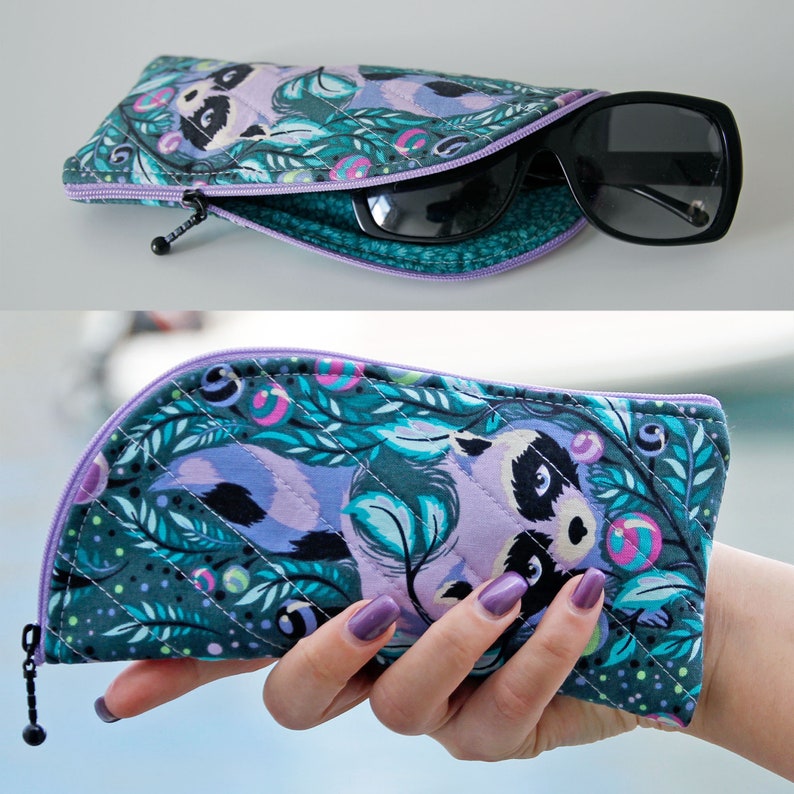 Pu&ograve; includere: Un astuccio per occhiali in tessuto trapuntato con una stampa di procioni color verde acqua e viola, dotato di chiusura a zip. L'astuccio ha una forma curva e contiene occhiali da sole neri. Il tessuto esterno presenta un motivo ripetitivo di procioni, foglie e piccoli accenti circolari nelle tonalit&agrave; del verde, verde acqua, viola e rosa.