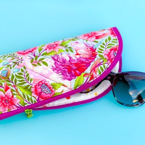 Pu&ograve; includere: Un astuccio per occhiali in tessuto trapuntato con un vivace motivo floreale e di unicorni nei toni del rosa, verde e bianco, rifinito con una cerniera color magenta brillante. Un paio di occhiali da sole con montatura scura &egrave; inserito nell'astuccio.