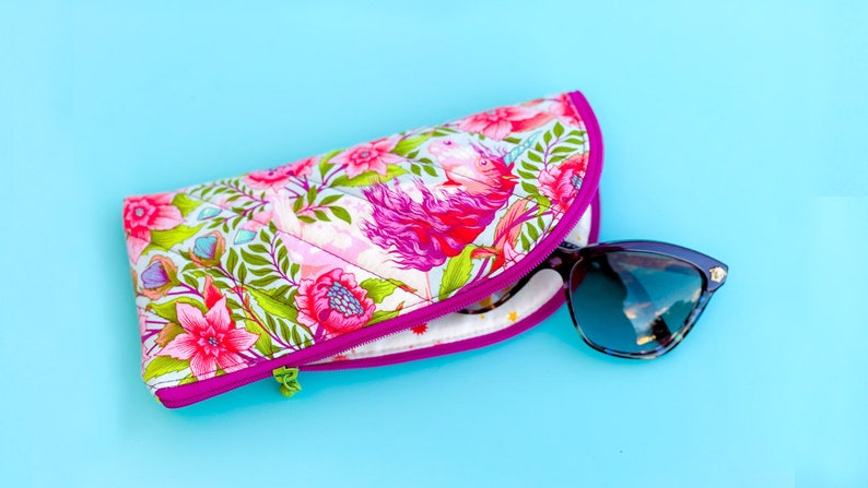 Pu&ograve; includere: Un astuccio per occhiali in tessuto trapuntato con un vivace motivo floreale e di unicorni nei toni del rosa, verde e bianco, rifinito con una cerniera color magenta brillante. Un paio di occhiali da sole con montatura scura &egrave; inserito nell'astuccio.