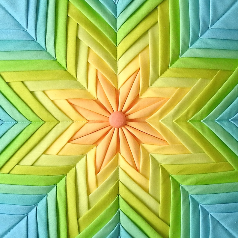 K&ouml;nnte beinhalten: Ein farbenfroher Stoff-Sternenstrahl mit einem zentralen Blumendesign. Der Sternenstrahl besteht aus mehreren Stoffschichten in Blaut&ouml;nen, Gr&uuml;n, Gelb und Orange. Die Blume in der Mitte ist hellorange mit einem rosa Zentrum.