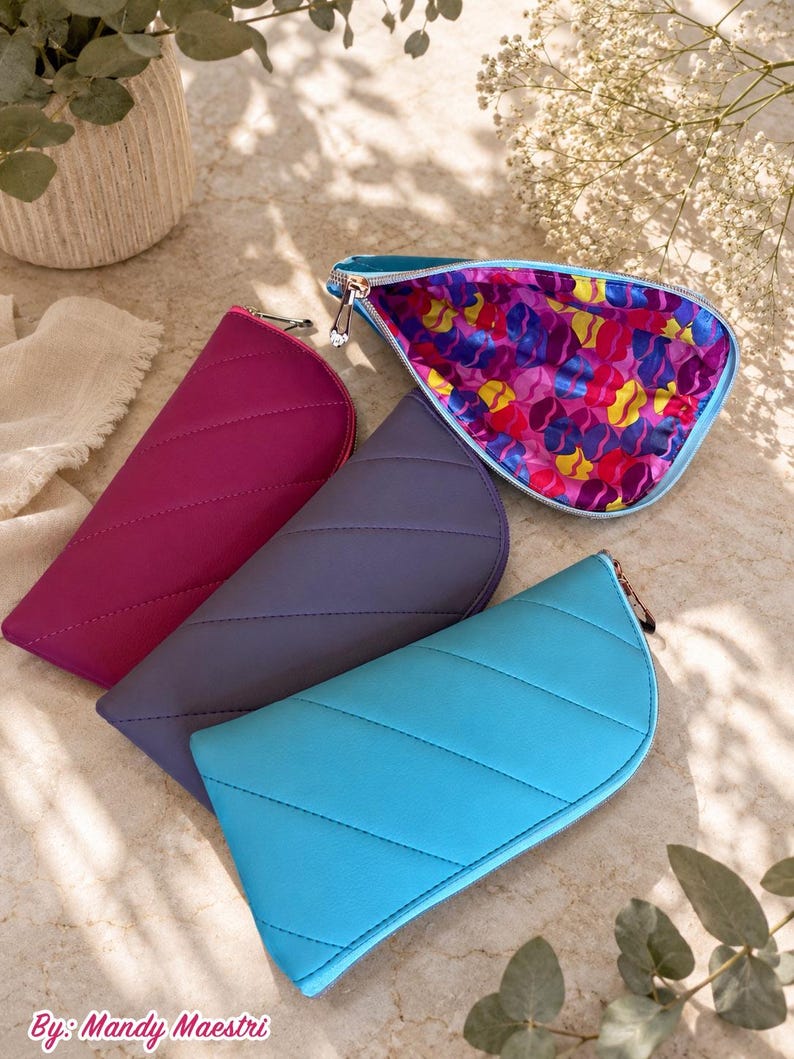 Pu&ograve; includere: Quattro pochette semicircolari con cerniera nei colori magenta, grigio scuro e blu brillante. Ogni pochette presenta cuciture trapuntate diagonali e una cerniera color argento. Una &egrave; aperta, rivelando una fodera interna con un motivo astratto.