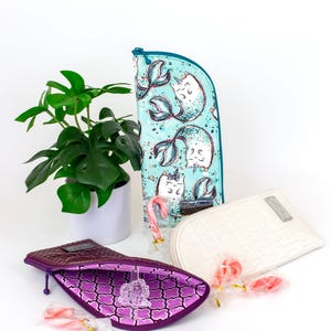 Pu&ograve; includere: Tre pochette con cerniera: una turchese con stampa di gatti sirena, una bianca tinta unita con trama intrecciata e una viola scuro con interno fantasia. Ogni pochette &egrave; accompagnata da un piccolo bastoncino di zucchero rosa e bianco.