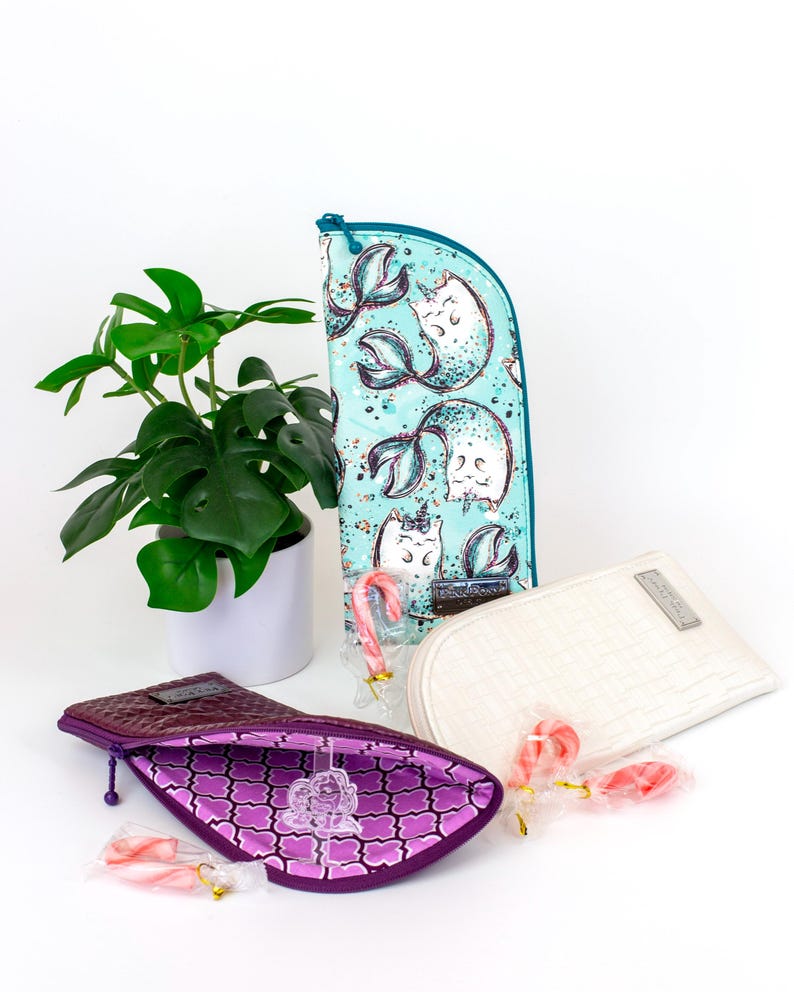 Pu&ograve; includere: Tre pochette con cerniera: una turchese con stampa di gatti sirena, una bianca tinta unita con trama intrecciata e una viola scuro con interno fantasia. Ogni pochette &egrave; accompagnata da un piccolo bastoncino di zucchero rosa e bianco.