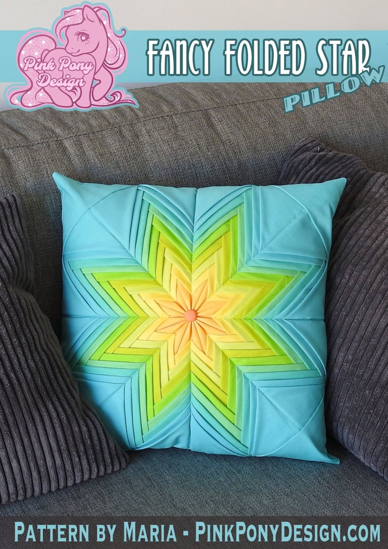 K&ouml;nnte beinhalten: Ein t&uuml;rkisfarbenes Kissen mit einem mehrfarbigen Sternmuster. Der Stern besteht aus gefaltetem Stoff in Gr&uuml;n-, Gelb- und Oranget&ouml;nen. Das Kissen liegt auf einem grauen Sofa. "FANCY FOLDED STAR PILLOW" steht in schwarzer Schrift oben im Bild. "PATTERN BY MARIA - PINKPONYDESIGN.COM" steht in schwarzer Schrift unten im Bild.