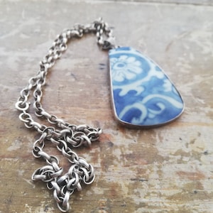 May include: A silver chain necklace with a blue and white ceramic pendant featuring a floral design.