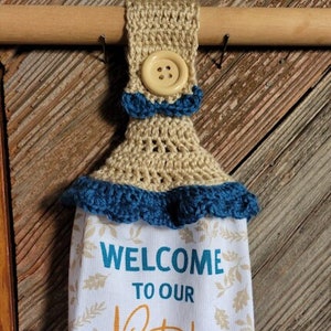 May include: A white kitchen towel with a blue and white plaid border. The towel features a blue truck with a bed full of pumpkins and the text "Welcome to our Patch" and "Pick your own pumpkins". The towel has a crocheted beige and blue hanging loop.