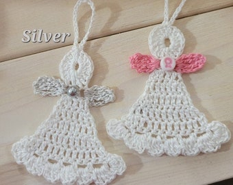 Puede incluir: Dos adornos de ángel de ganchillo, uno con una cuenta plateada y el otro con una cinta rosa y una cinta rosa de concienciación sobre el cáncer de mama. Los adornos están sobre una superficie de madera con las palabras "Silver" y "Breast Cancer" escritas en la superficie.