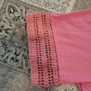 May include: Pink crocheted trim on a pink shirt. The trim is a delicate, openwork design.