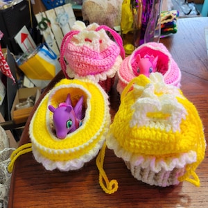 May include: Three crocheted drawstring bags in pink, yellow, and white with a ruffle trim. Each bag has a small plastic toy pony inside.